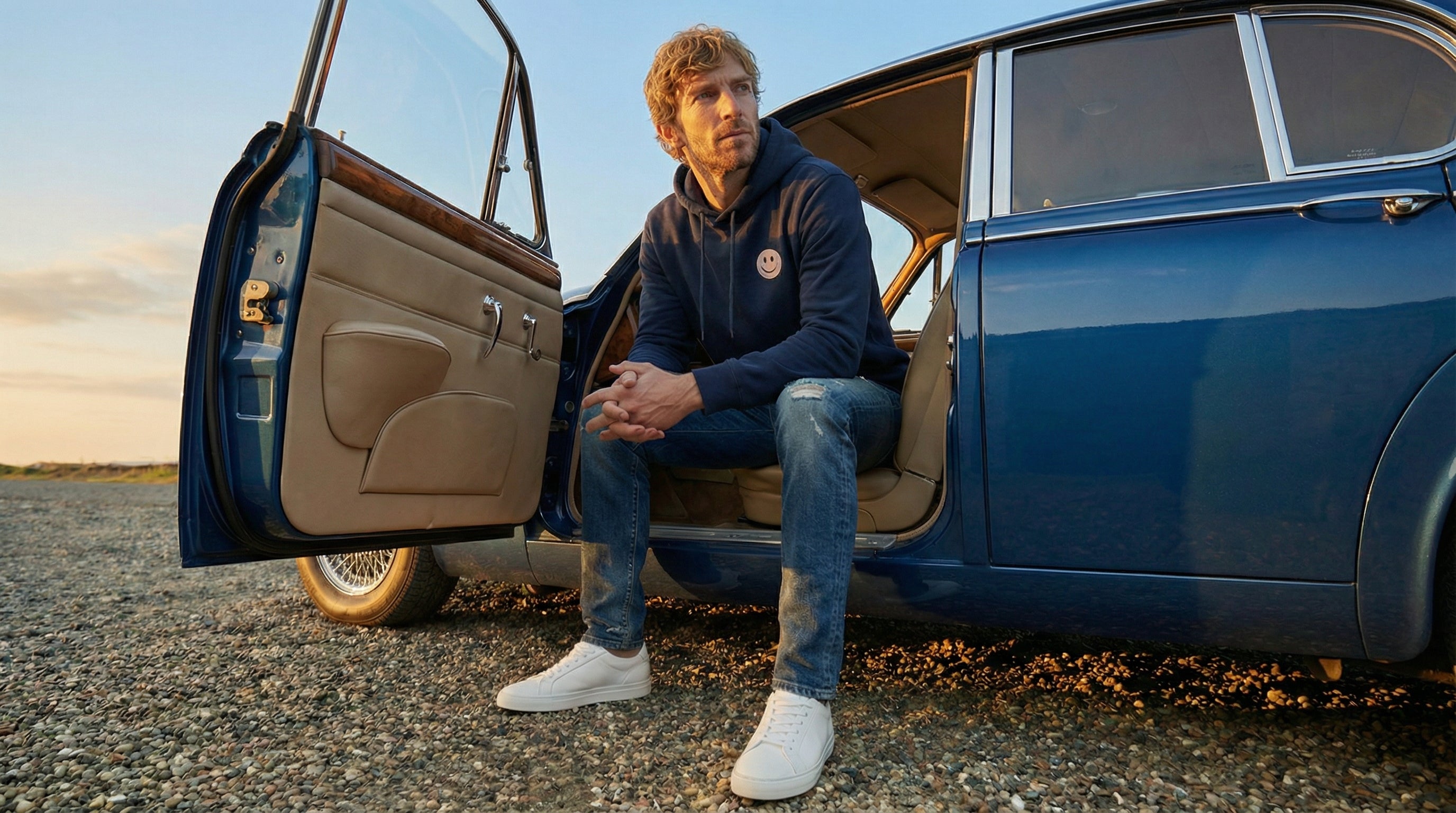 Man sitting in an open door of a vintage car with a scenic background